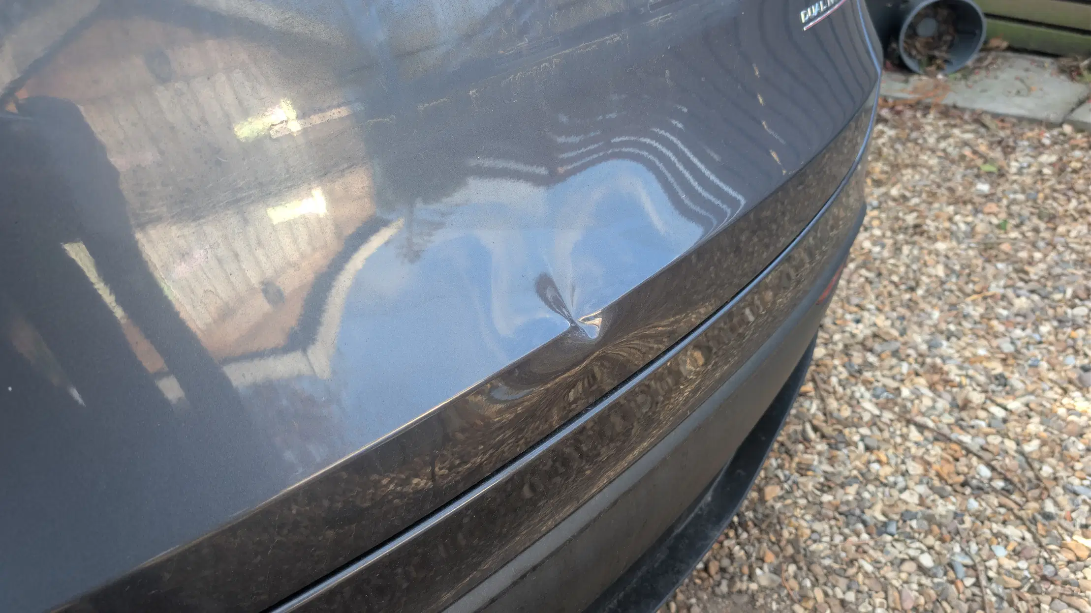 Close-up of a dent in the grey Tesla tailgate before repair